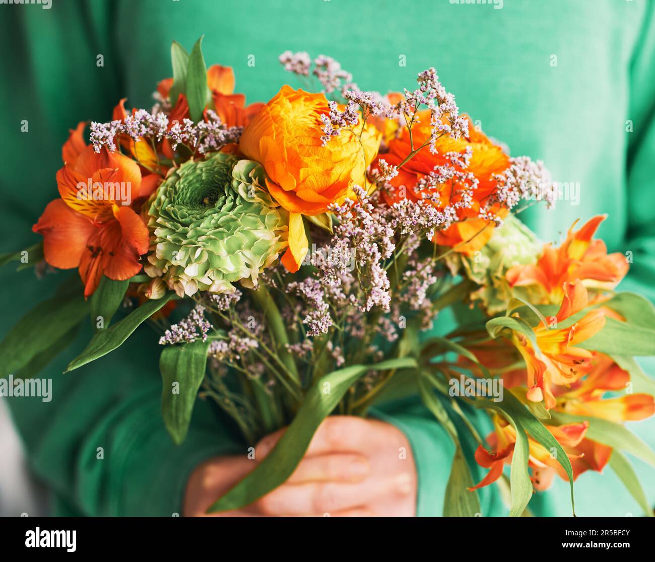 Close up portrait of beautiful green and orange ranunculus and alstroemeria bouquet holding by a person Stock Photo