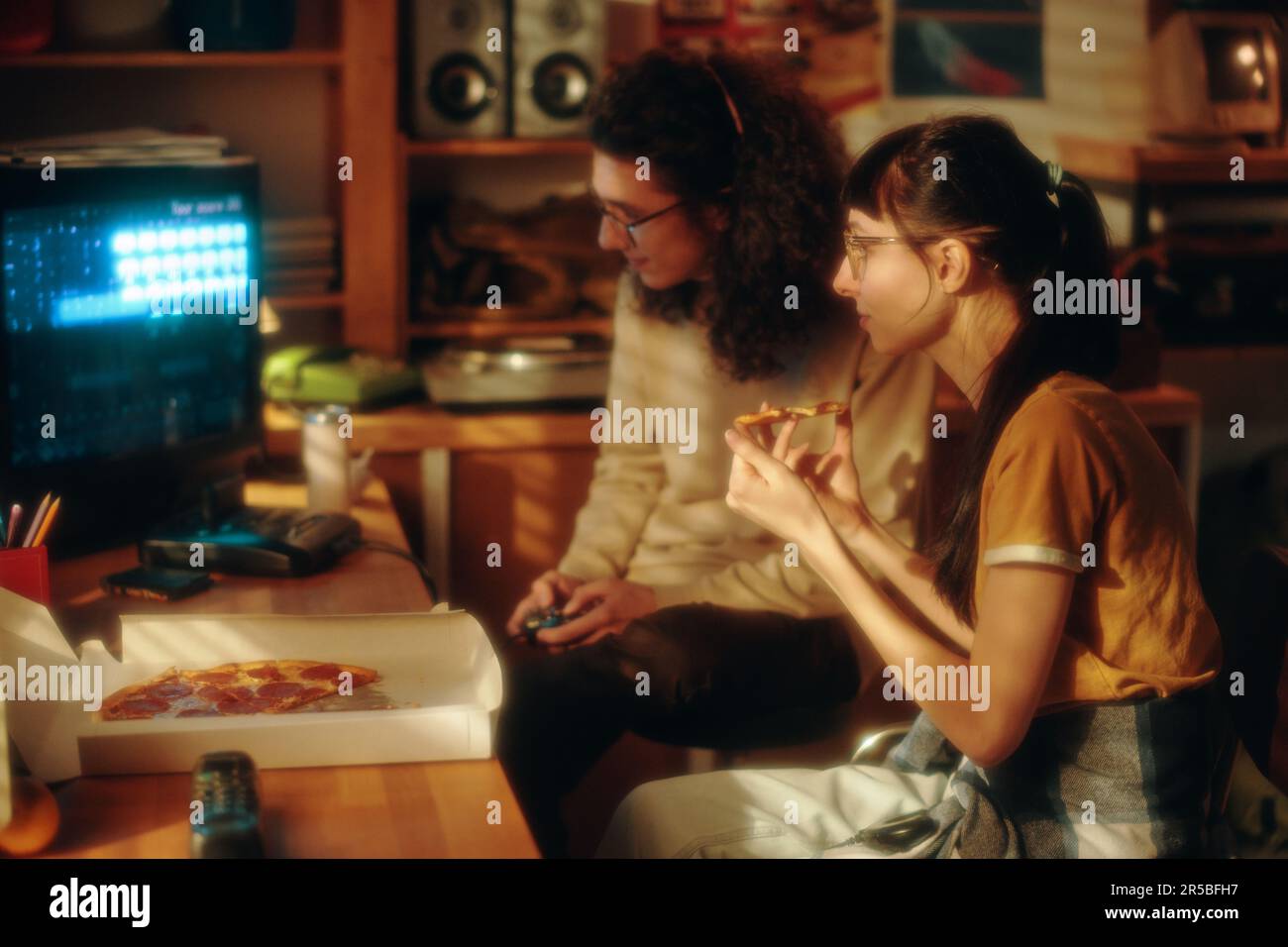 Teenage boy playing video game while girl eating pizza and watching for
