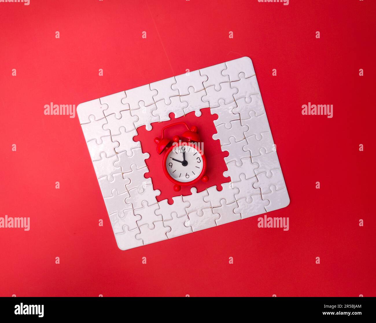 An alarm clock sitting atop a bright red jigsaw puzzle piece against a