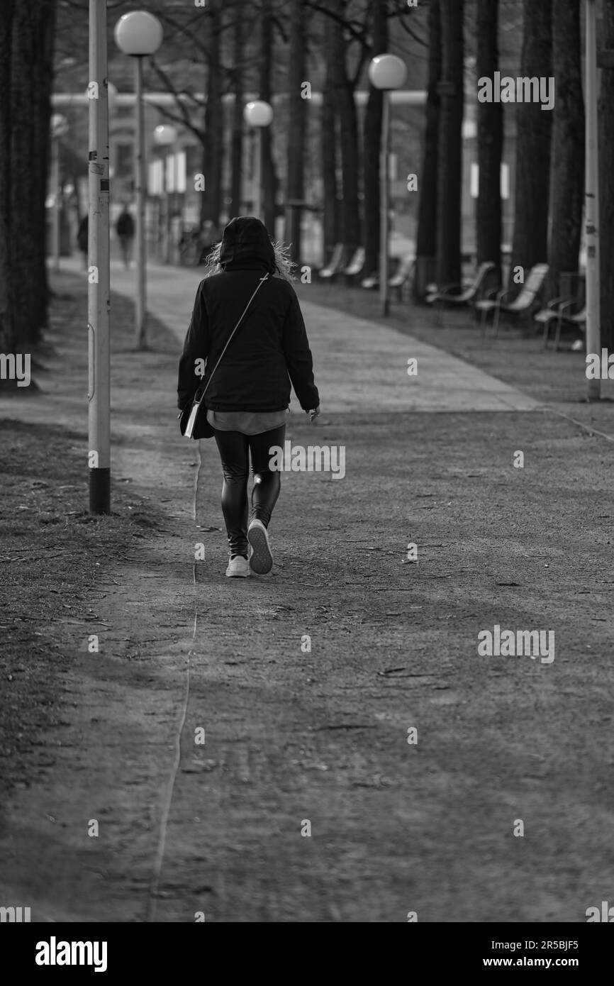 A grayscale of a female figure strolling along a pathway Stock Photo ...