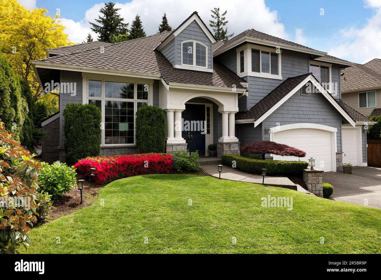Home exterior with blooming flowers and trees with lush green grass front lawn or yard Stock Photo