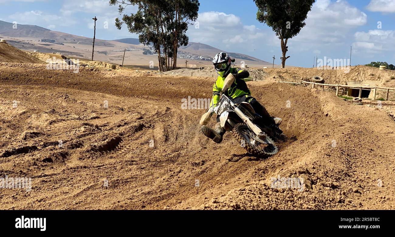 A male in a fullbody riding suit is seen riding a dirt bike on a