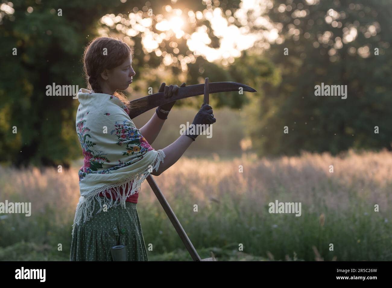 A woman dressed in traditional working outfit sharpens the scythe