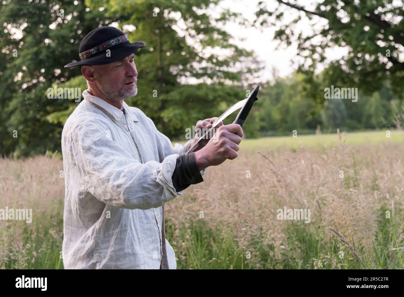 A man dressed in traditional working outfit sharpens the scythe during