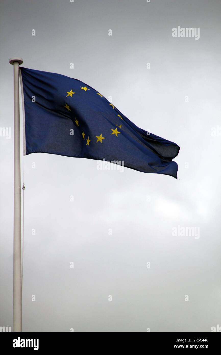 A vivid European Union (EU) flag waving in the wind against a cloudy sky backdrop, symbolizing unity and strength Stock Photo
