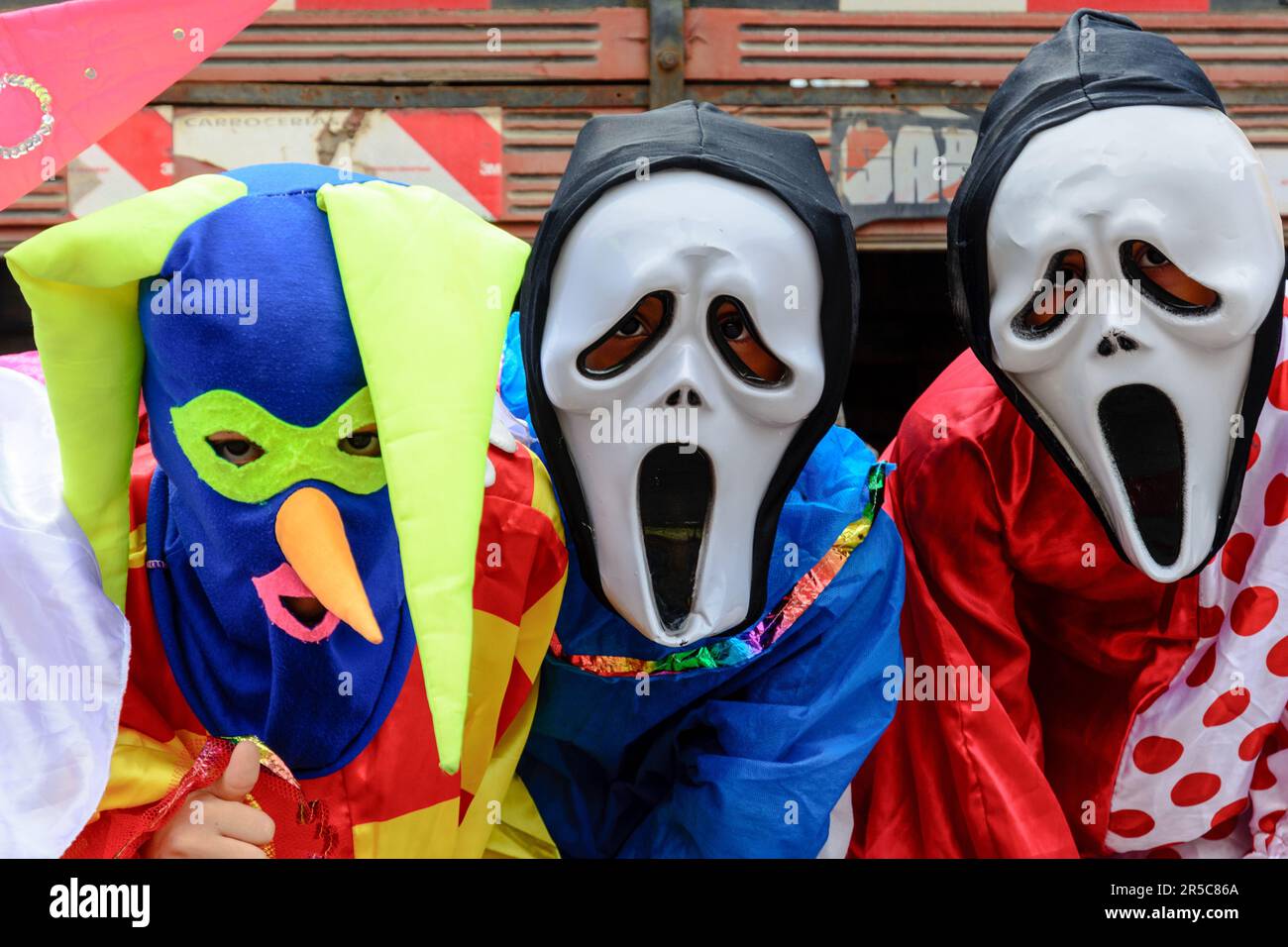 Two adult males wearing costume masks and cape accessories, each holding a colorful umbrella in