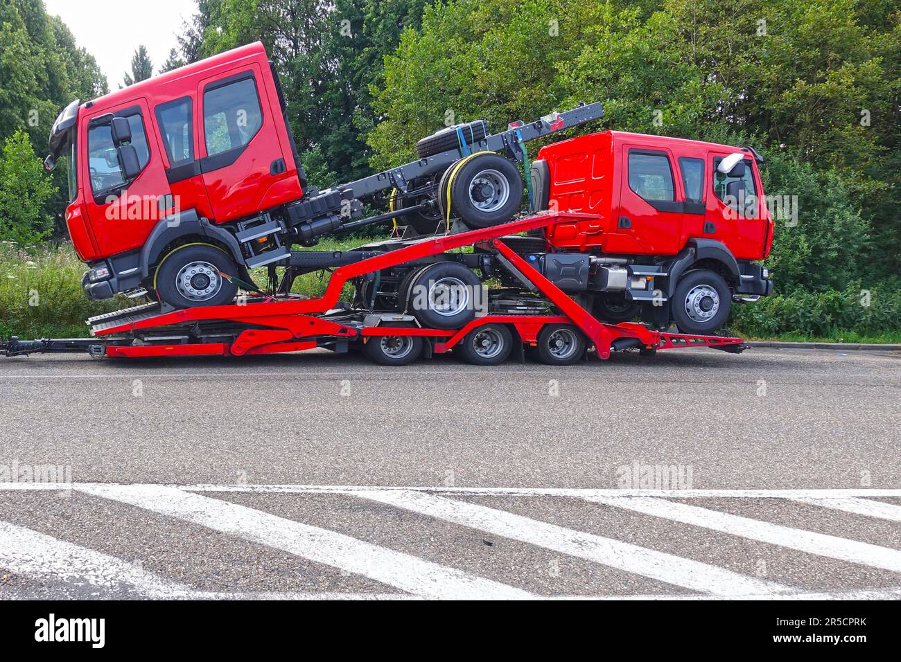 Truck carrier trailer transporting two brand-new trucks of red color. Stock Photo
