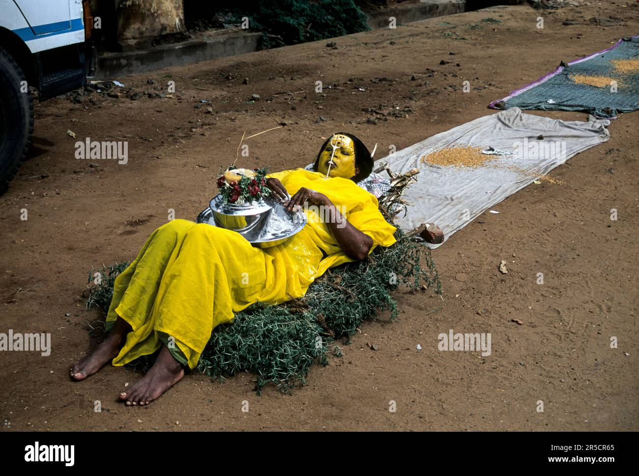 A woman begging lying on a bed of thorns in front of temple, Tamil Nadu