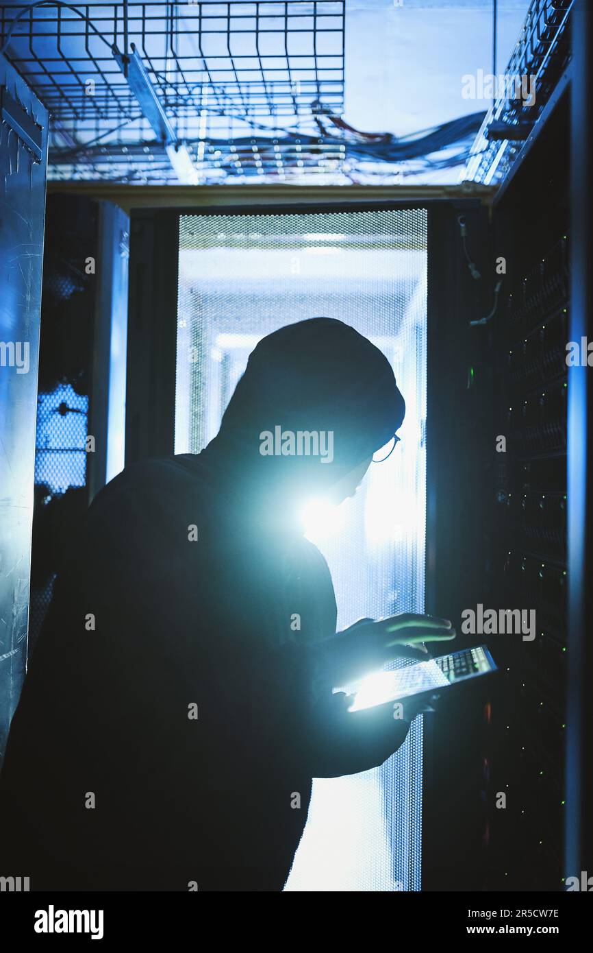I work best in the dark. a hacker using a digital tablet in a server room. Stock Photo