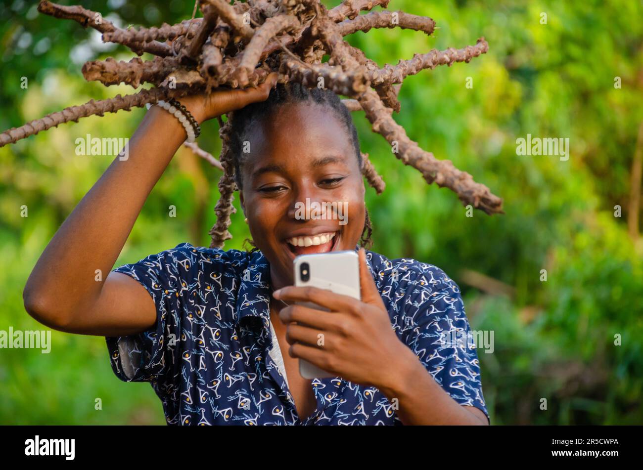 young African girl carrying wood and a and using her phone on a farm Stock Photo