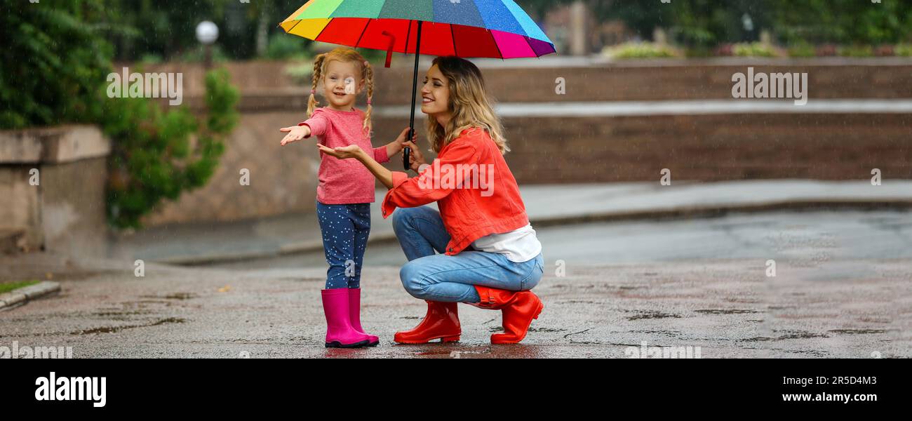 Happy mother and daughter with bright umbrella under autumn rain ...