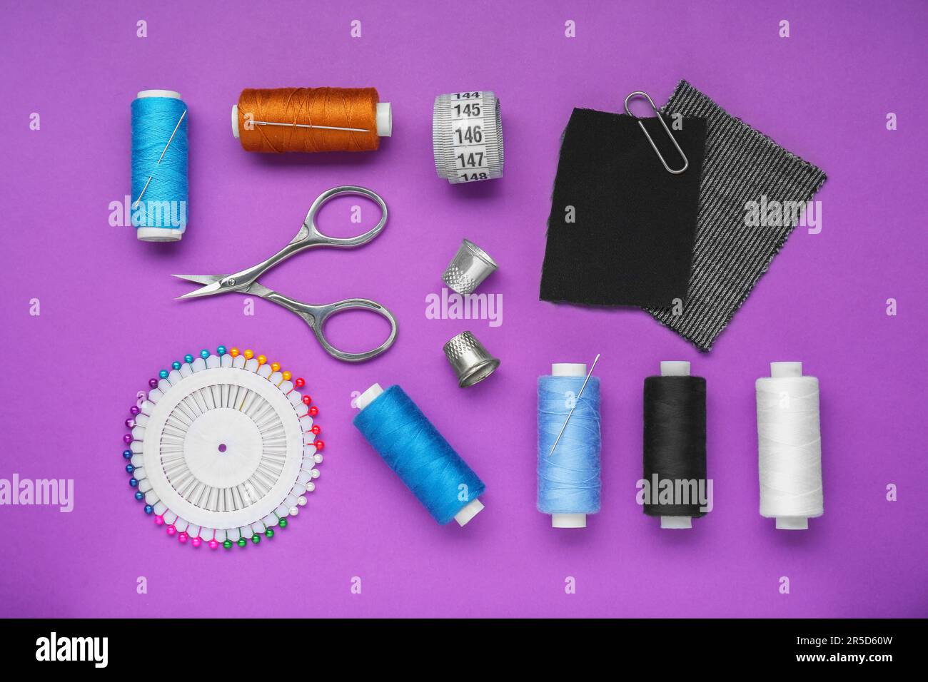Flat lay composition with thimbles and different sewing tools on purple background Stock Photo