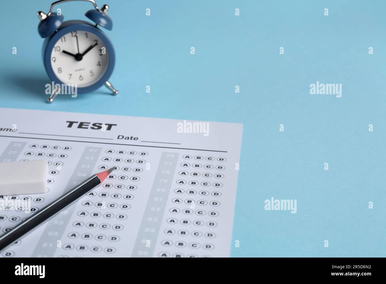 Answer sheet, pencil and alarm clock on light blue background, space