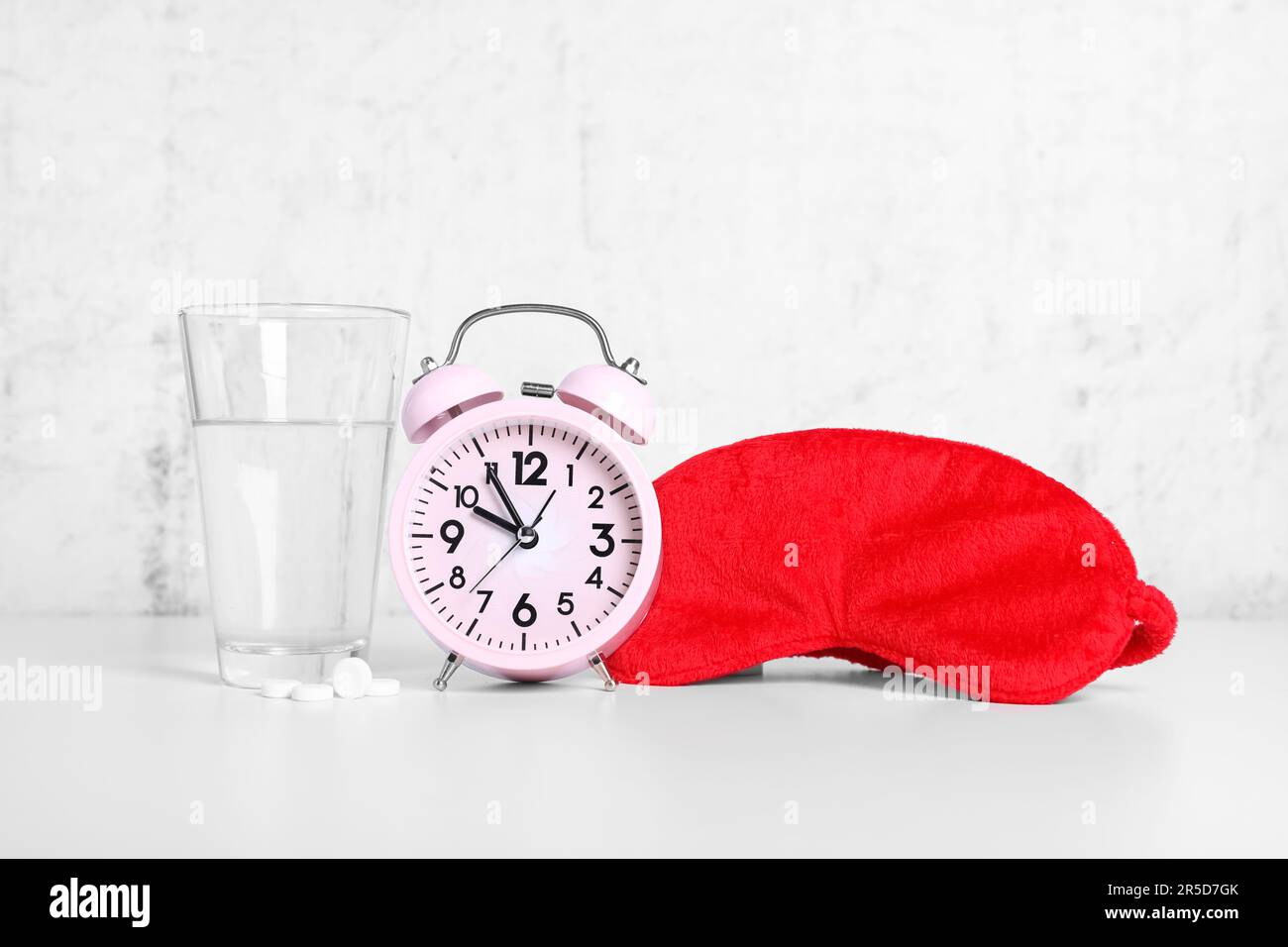 Red sleep mask, glass of water, pills and alarm clock on white table Stock Photo