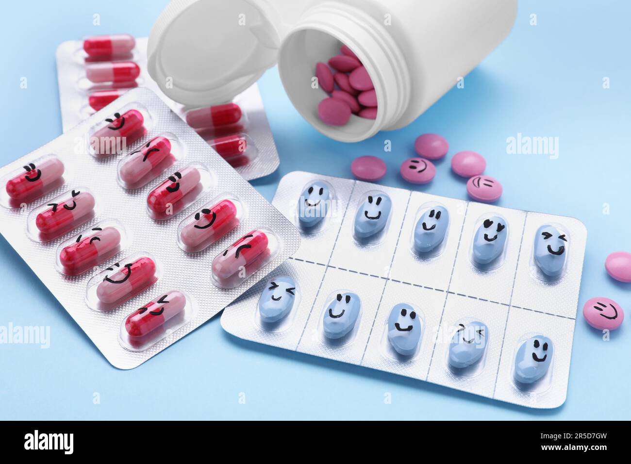 Blister, bottle and antidepressant pills with funny faces on light blue ...