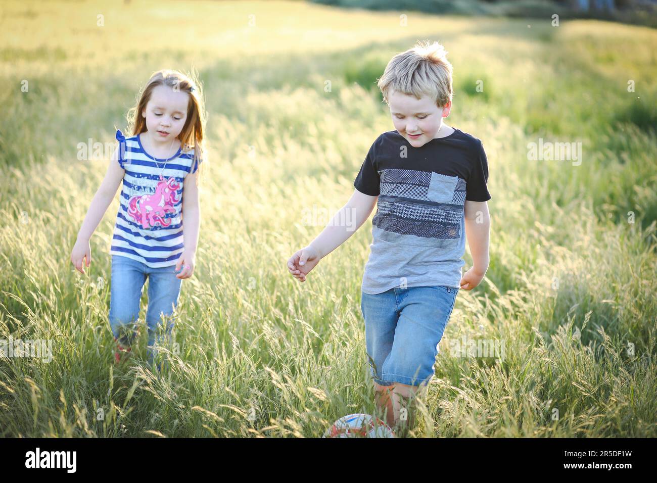 Boy and girl running through long grass playing soccer at the park
