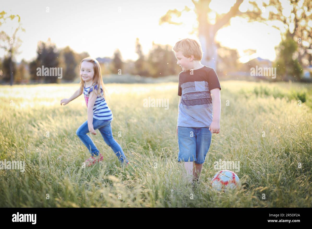 Boy and girl running through long grass playing soccer at the park