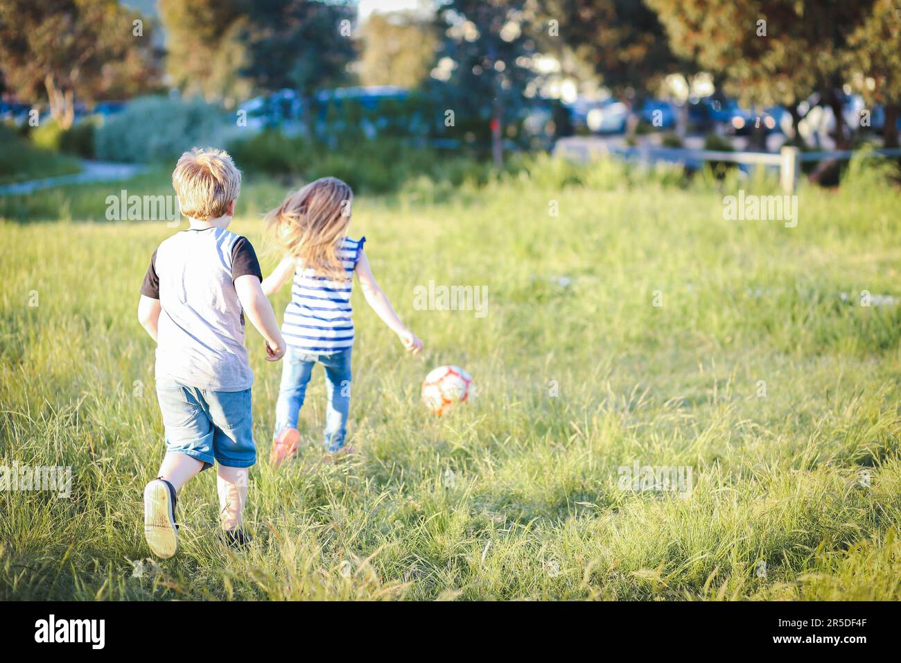 Boy and girl running through long grass playing soccer at the park