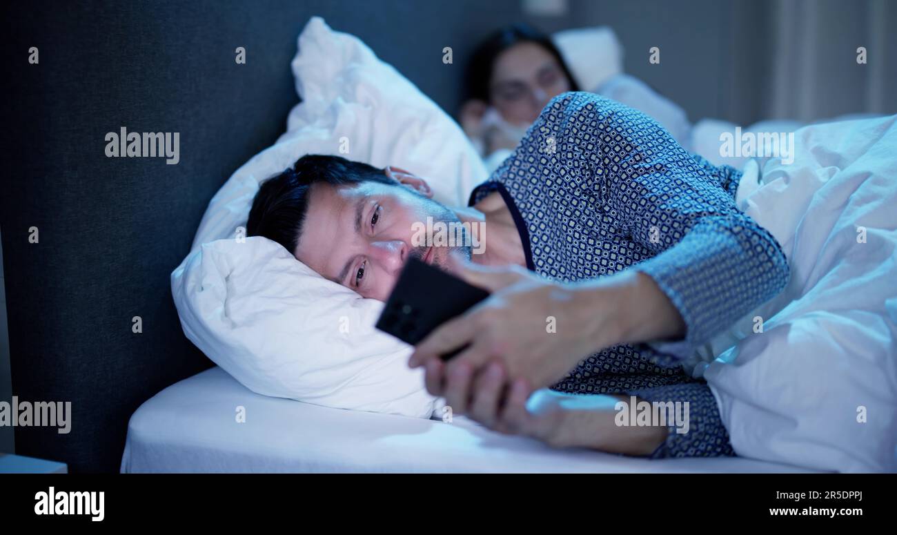 Young Man Using Cellphone While Her Wife Sitting On Bed At Night Stock Photo