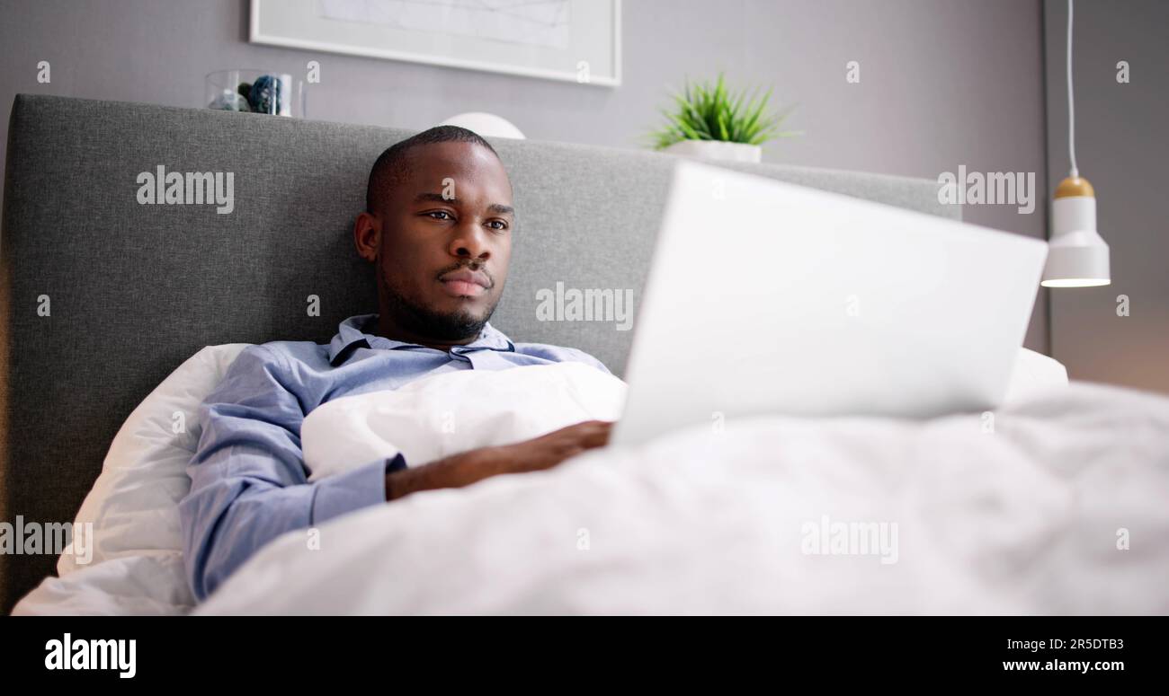 Happy Man Sitting On Bed Using Laptop Stock Photo