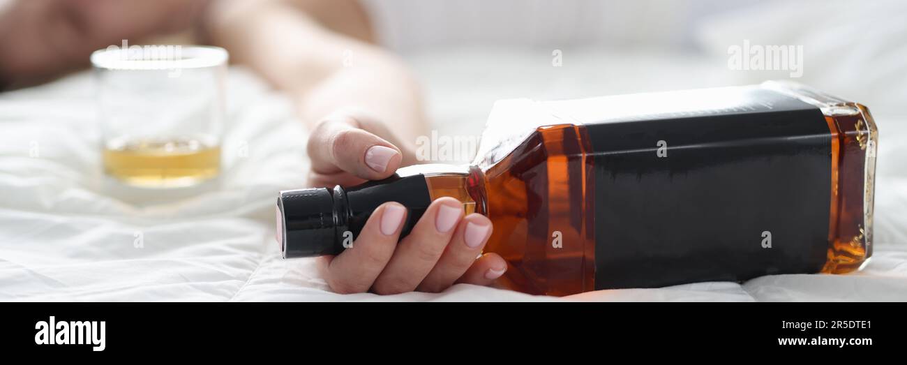 Woman is lying in bed dead drunk holding almost empty bottle of booze