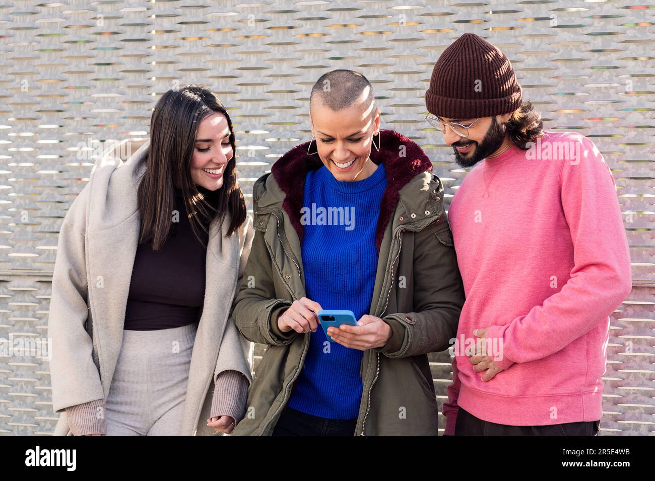 three smiling young friends enjoying using phone Stock Photo
