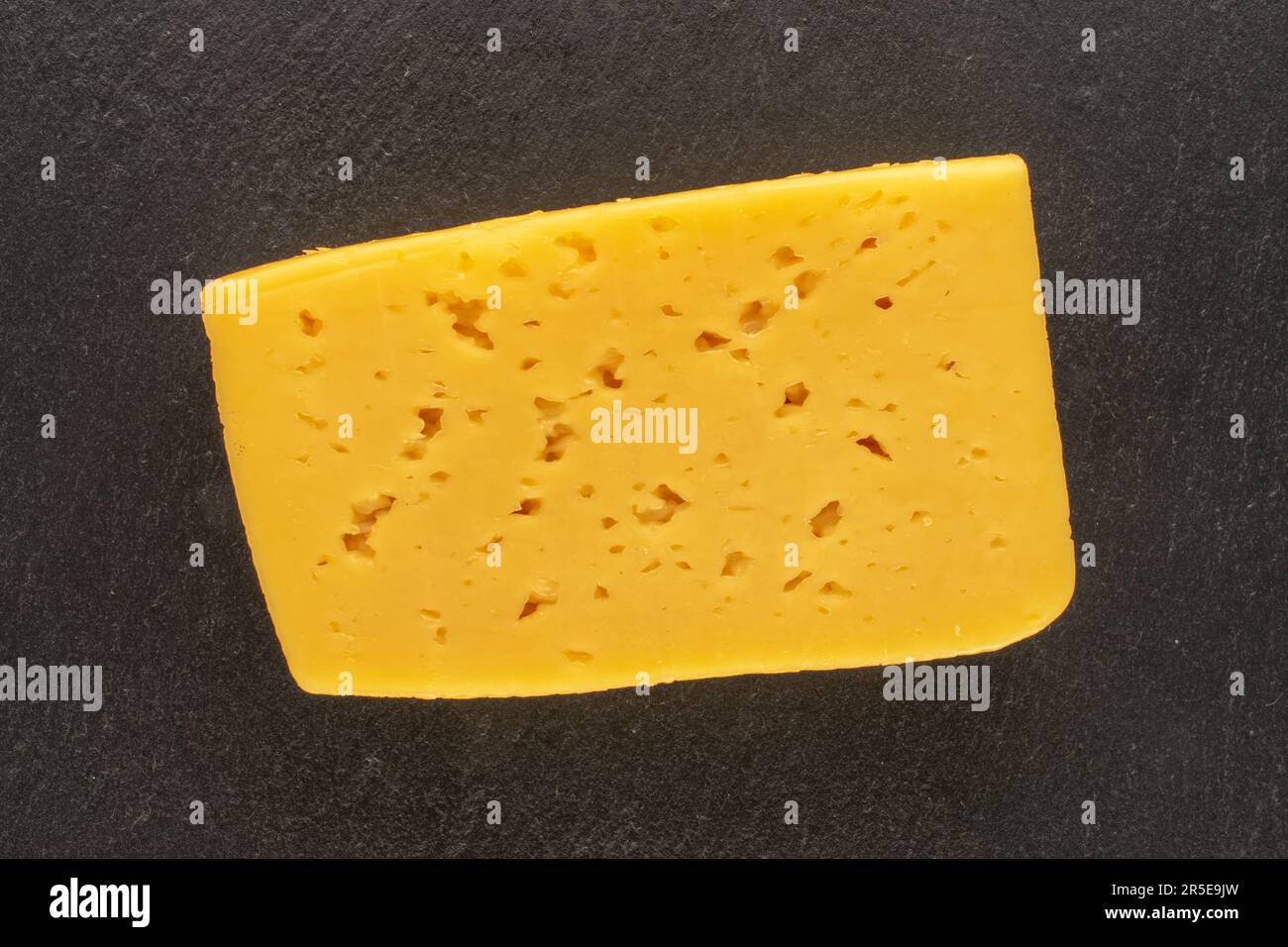 One piece of cheese on slate stone, macro, top view. Stock Photo