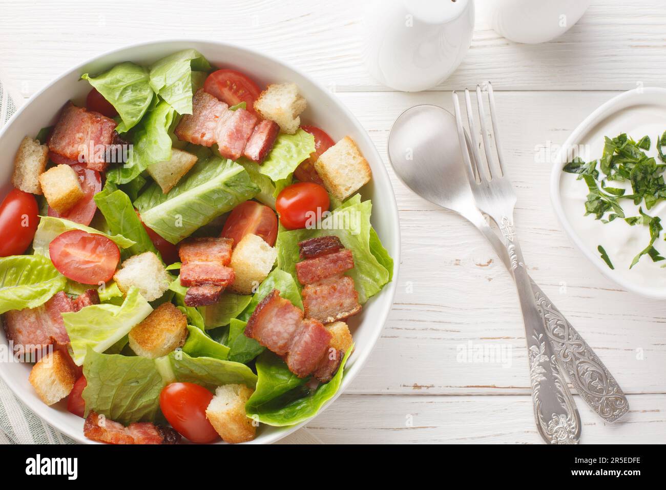 BLT salad with romaine lettuce, pieces of crispy bacon, tomatoes, crunchy croutons, and a creamy garlic dressing closeup on the plate on the table. Ho Stock Photo
