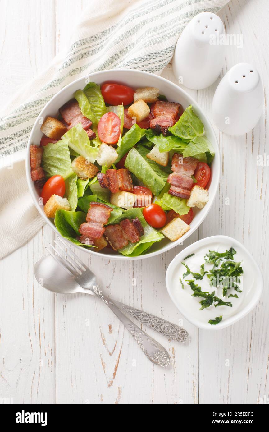 Bacon Lettuce Tomato, BLT salad with creamy dressing sauce, croutons closeup on the plate on the table. Vertical top view from above Stock Photo
