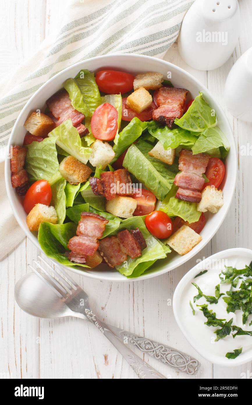BLT salad is loaded with fresh lettuce, crispy bacon, bright tomatoes croutons closeup on the plate on the table. Vertical top view from above Stock Photo