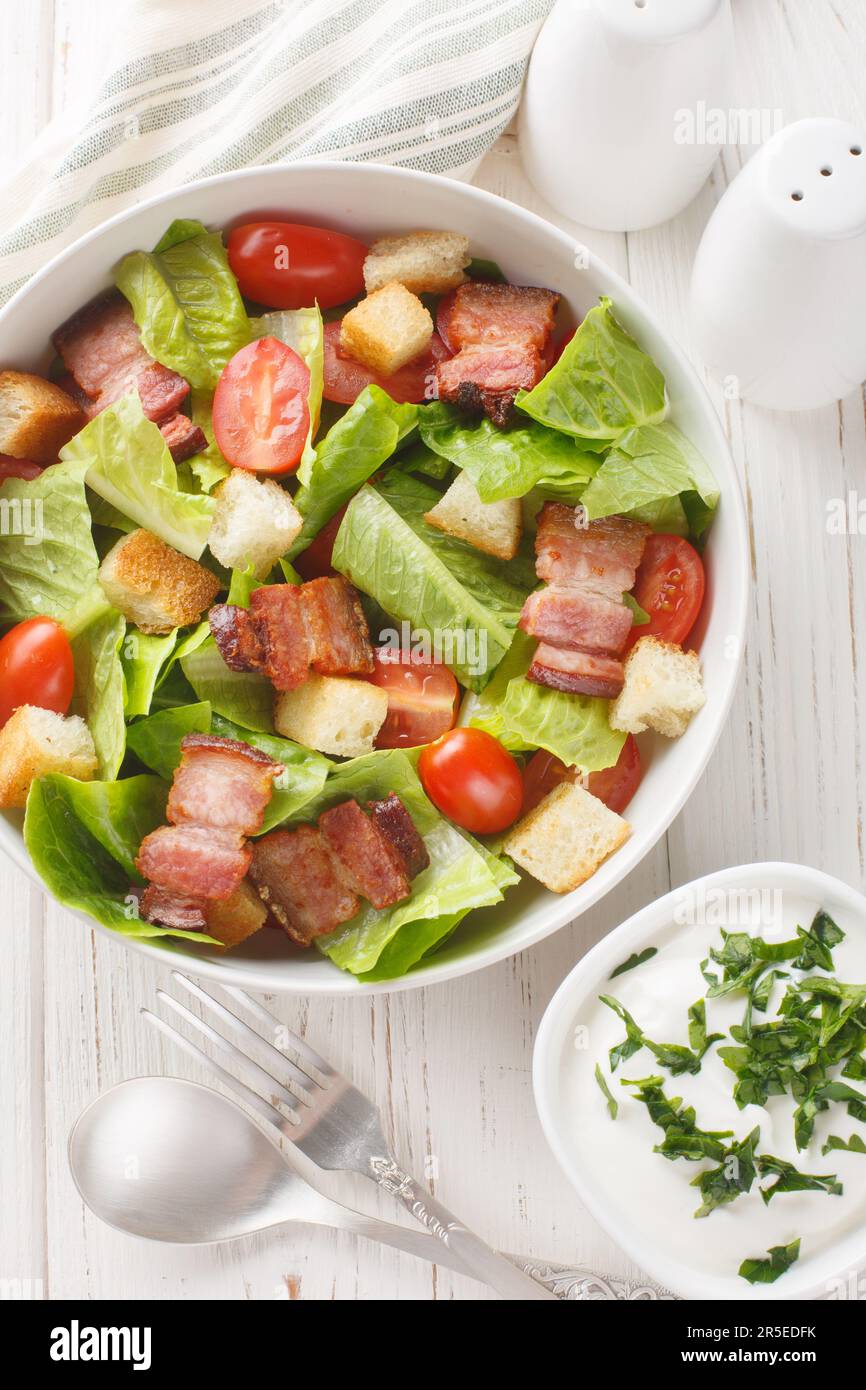 Classic american bacon blt salad with Lettuce, croutons and Tomato closeup on the plate on the table. Vertical top view from above Stock Photo