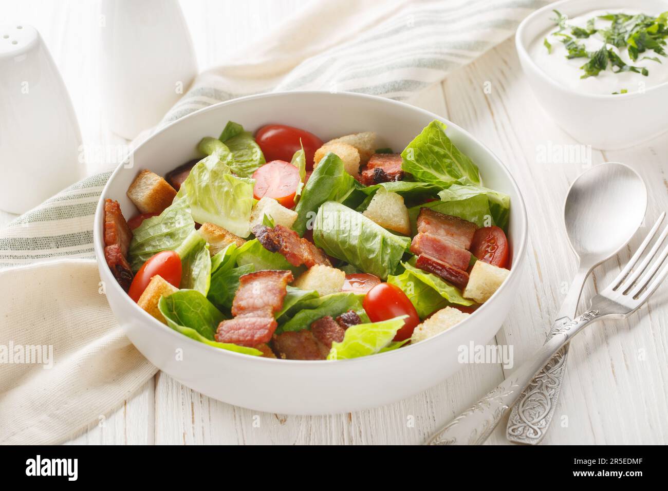 BLT Salad has a homemade ranch dressing, crispy bacon, croutons, lettuce and tomato closeup on the plate on the table. Horizontal Stock Photo
