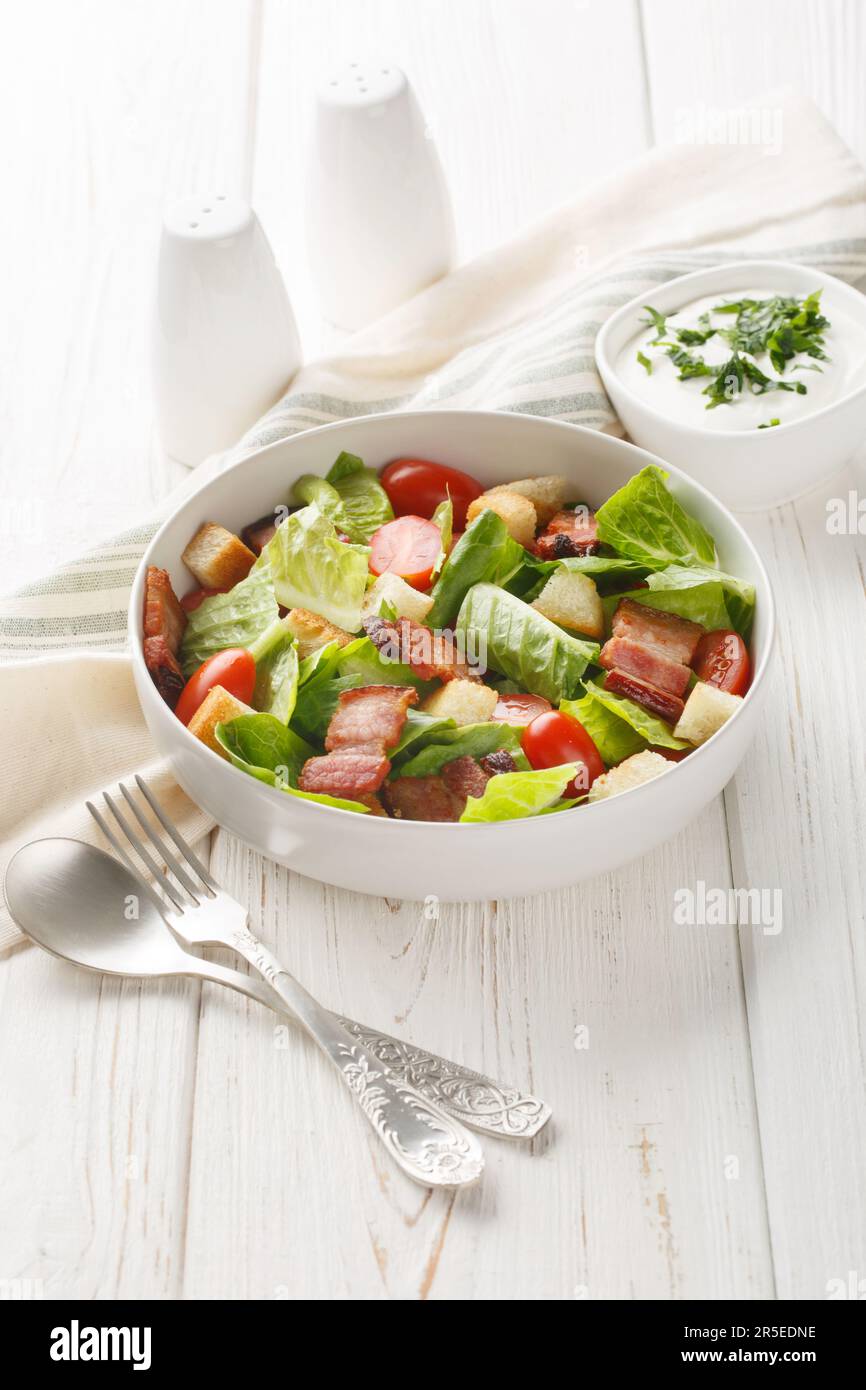 BLT salad is loaded with fresh lettuce, crispy bacon, bright tomatoes croutons closeup on the plate on the table. Vertical Stock Photo