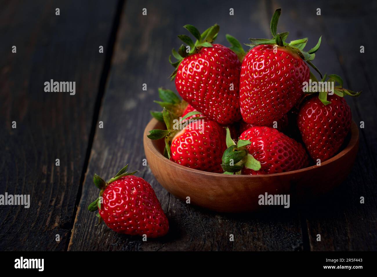 Berries of red strawberries in a wooden bowl on a dark wooden table Stock Photo