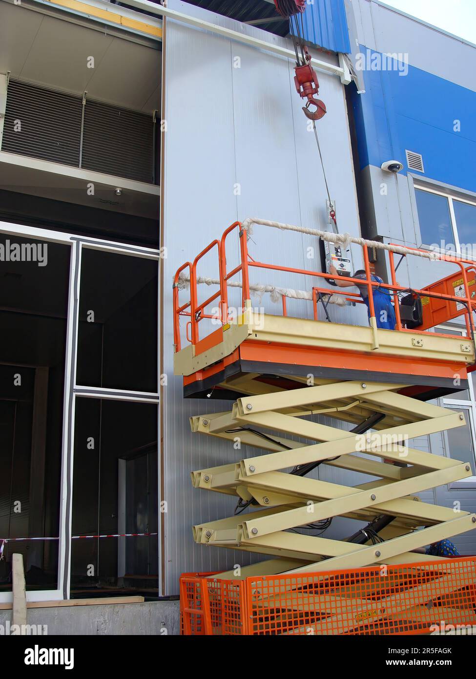 Worker operating Scissor lifts, installing wall panels using a suction cup. Warehouse
