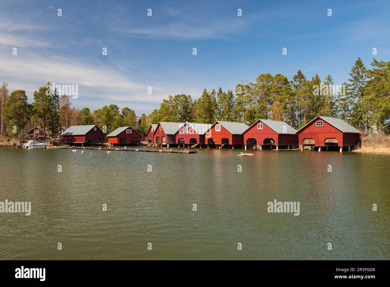 Nice red boathouses in a small bay by the Trollharen fishing location in Ljusne Halsingland Sweden with forest and a blue sky in background. Stock Photo
