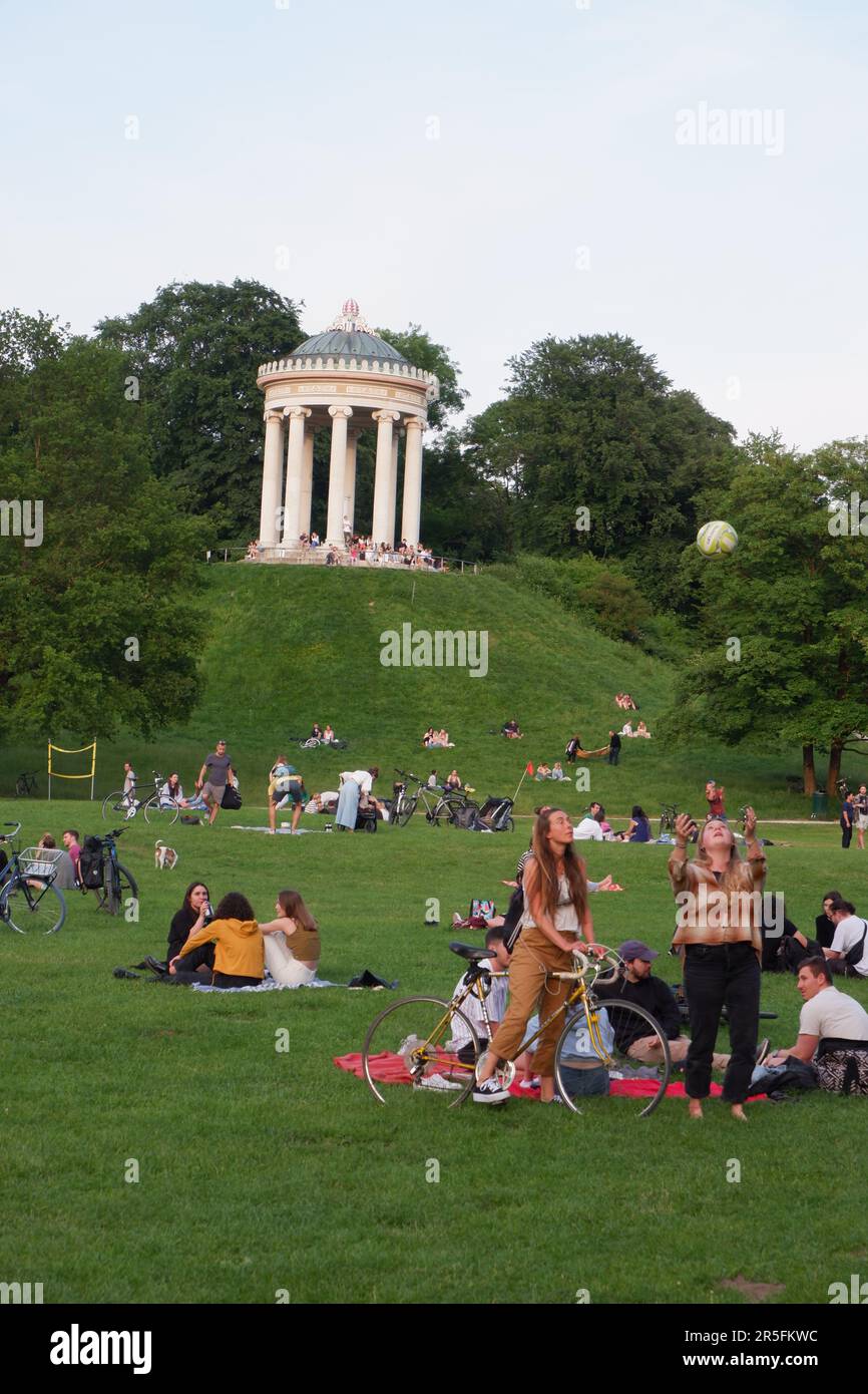 Crowds of people hanging out in the Englischer Garten English Garden Munich Germany with the Monopteros stone temple in background Stock Photo