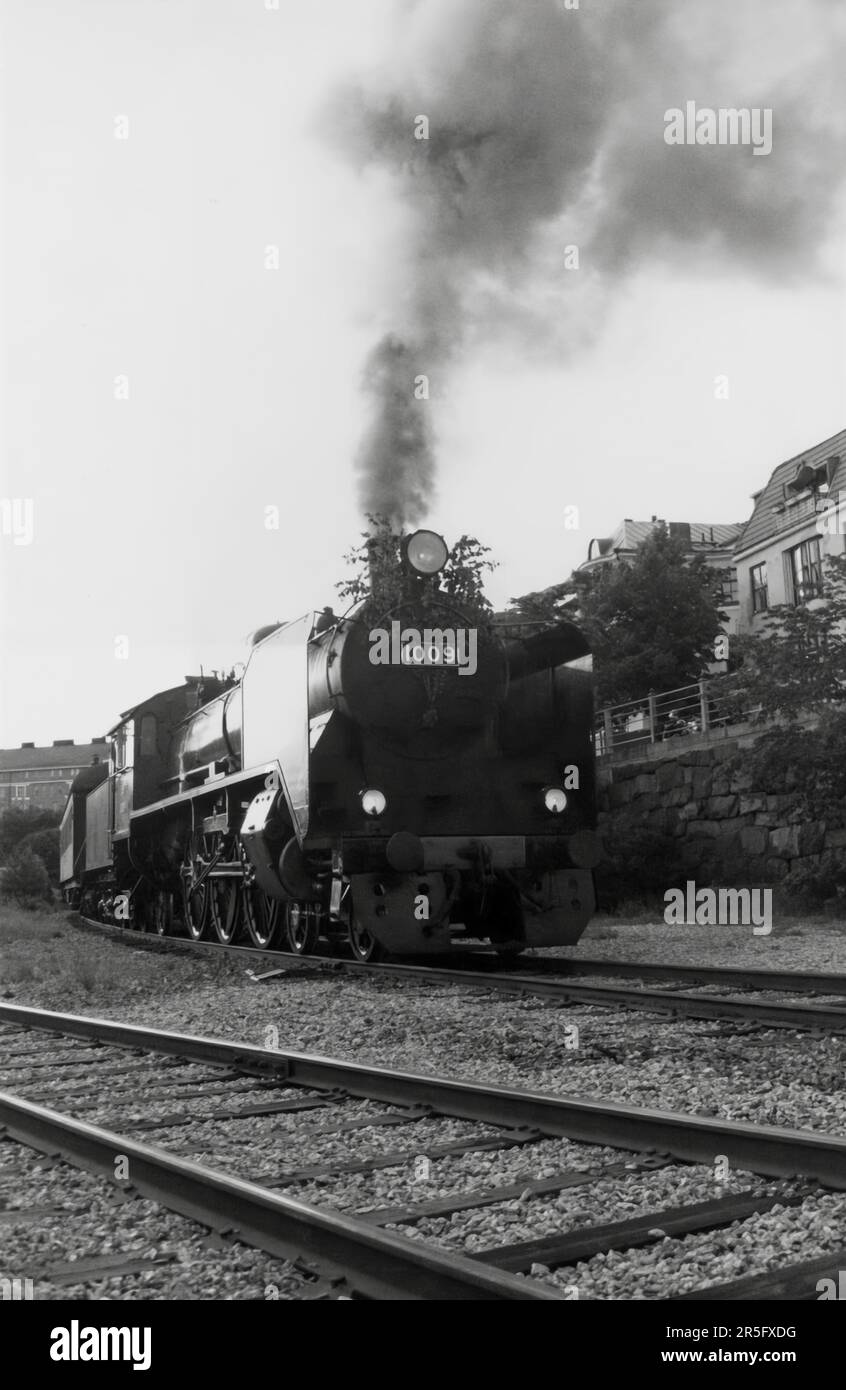 Hr1 class passenger express steam locomotive 1009 pulling a train in Eira, Helsinki, before this part of the Helsinki harbour rail line was dismantled in the 1990s. Merikatu buildings in the background. Stock Photo