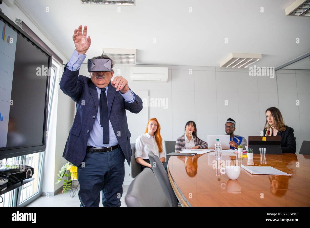 During a conference a businessman uses virtual reality headsets while others observe him Stock Photo