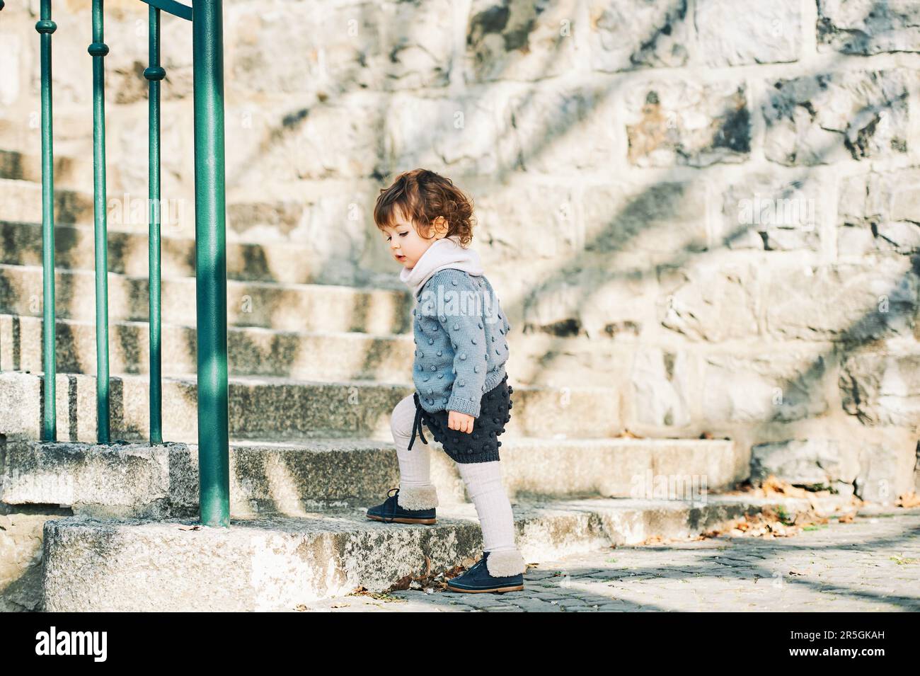 Outdoor portrait of adorable toddler girl walking up the stairs, child