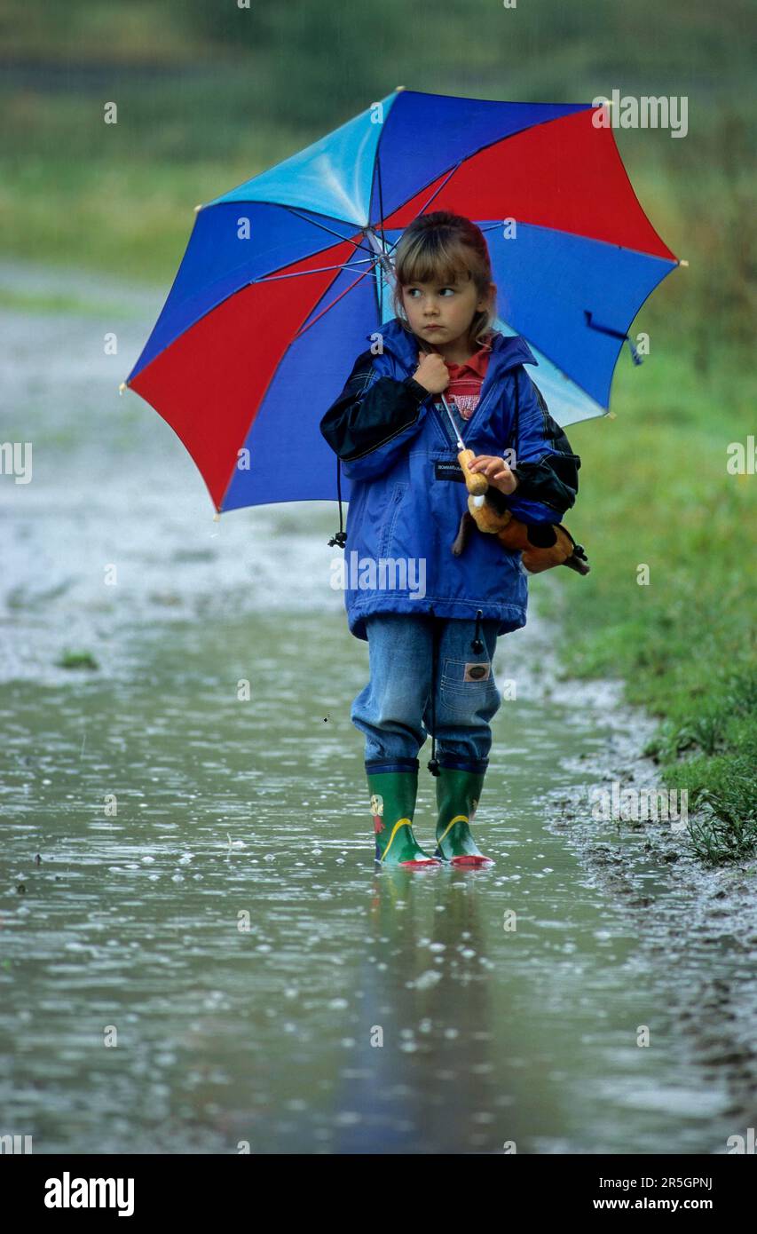 Little girl with umbrella and rubber boots standing in huge rain puddle in rainy weather Stock Photo