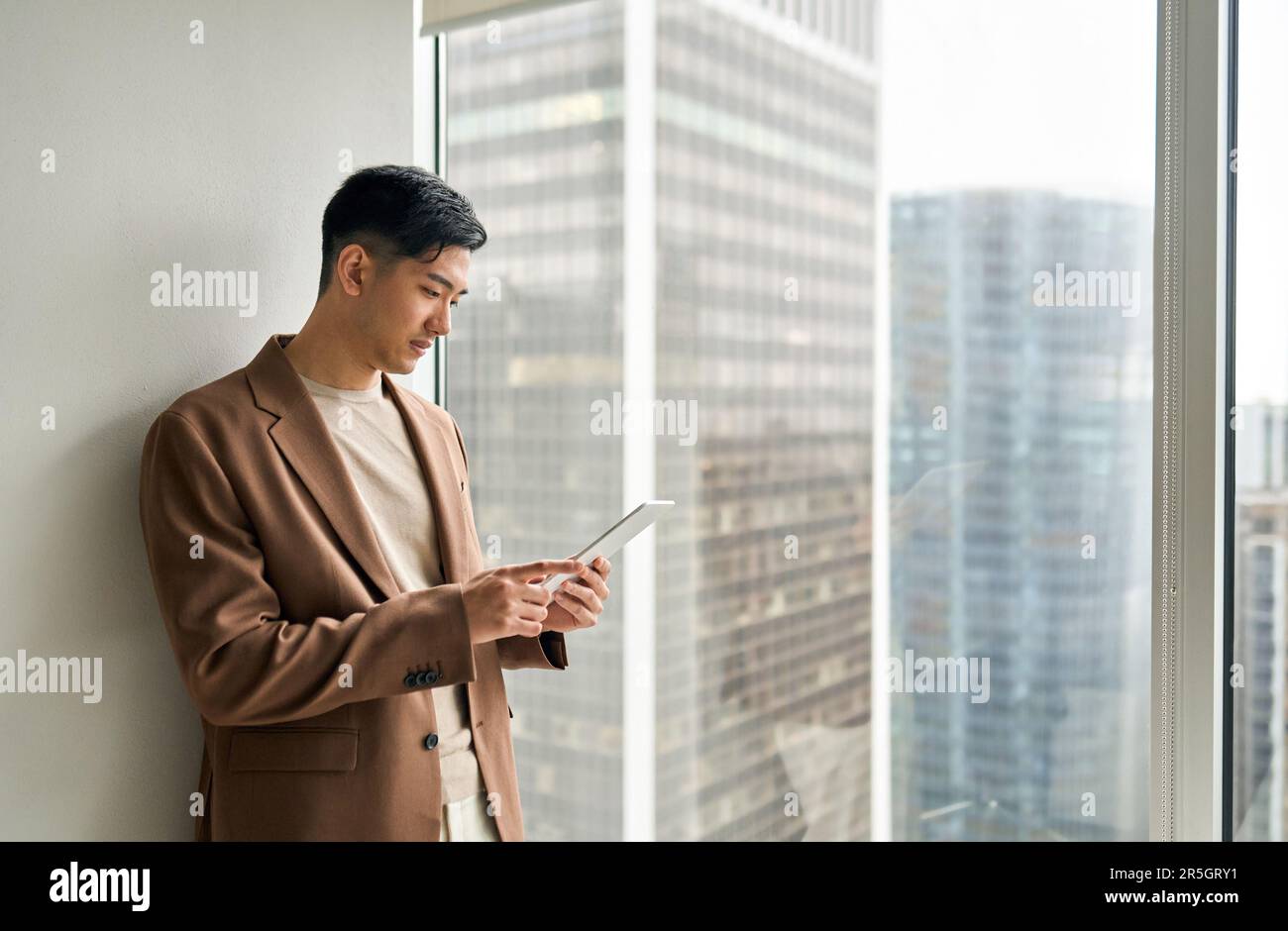 Professional young Asian businessman using tablet standing at window. Stock Photo