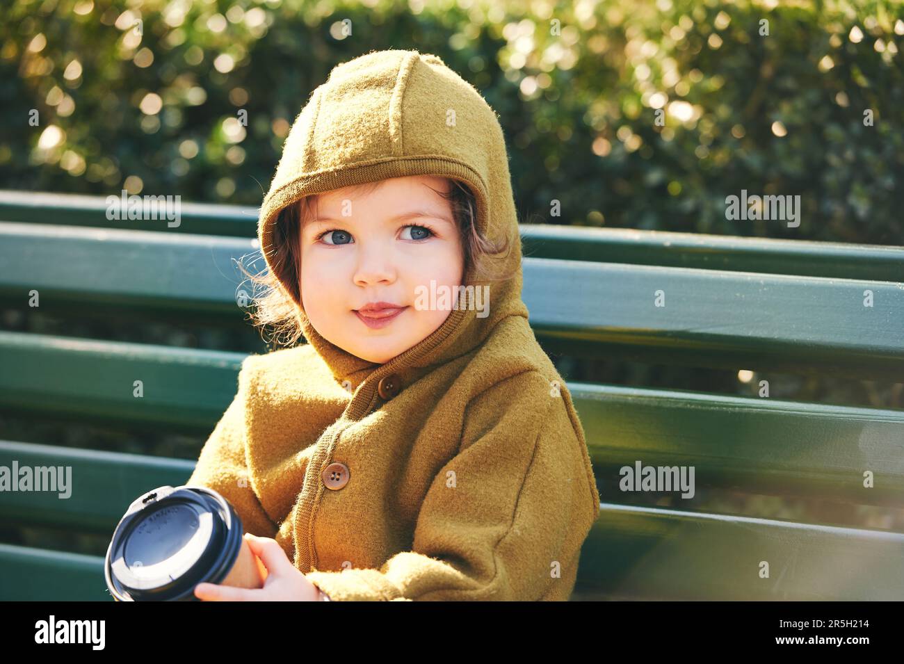 Funny toddler kid resting on bench, holding paper cup of take away coffee Stock Photo