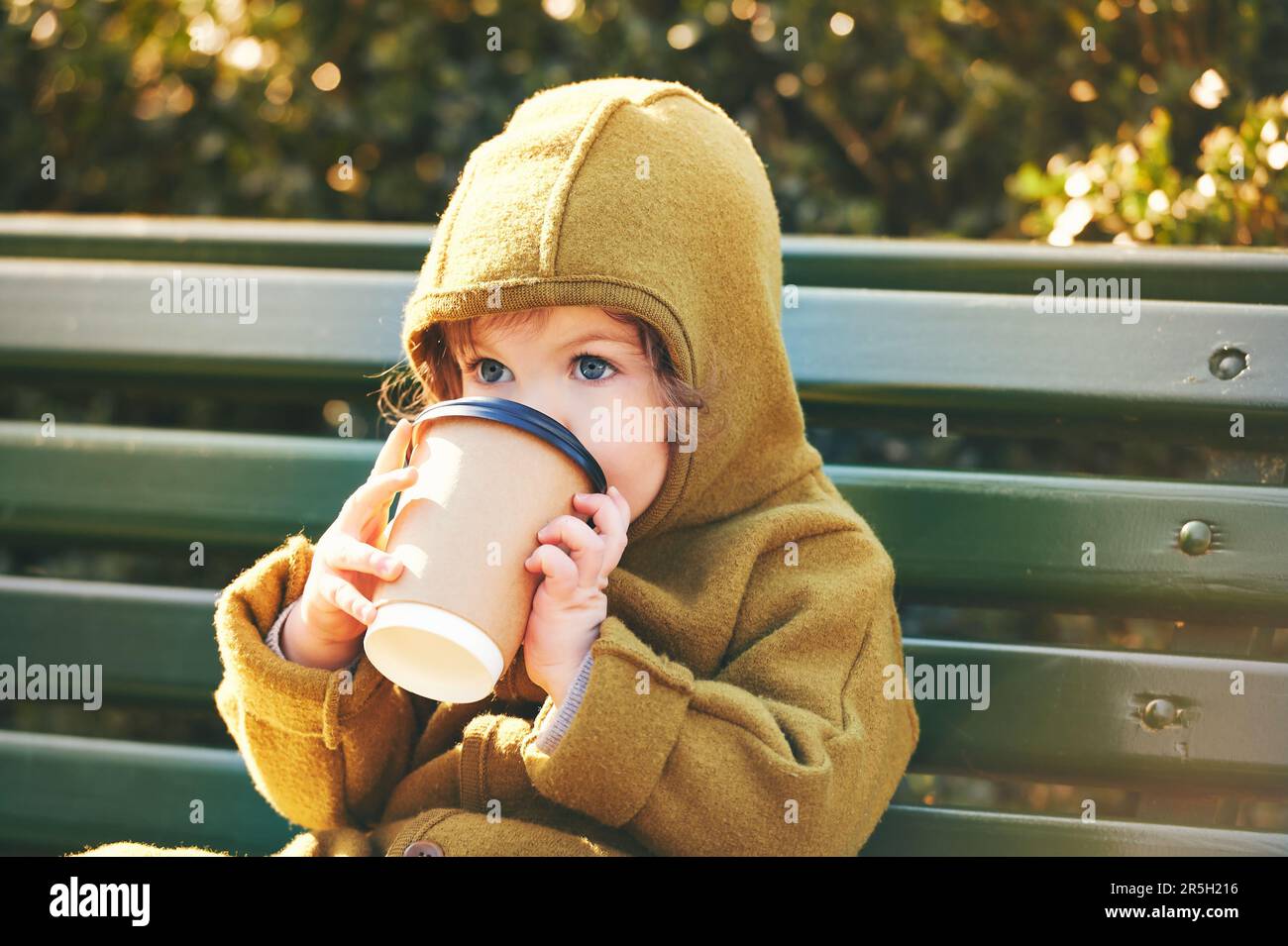 Funny toddler kid resting on bench, holding paper cup of take away