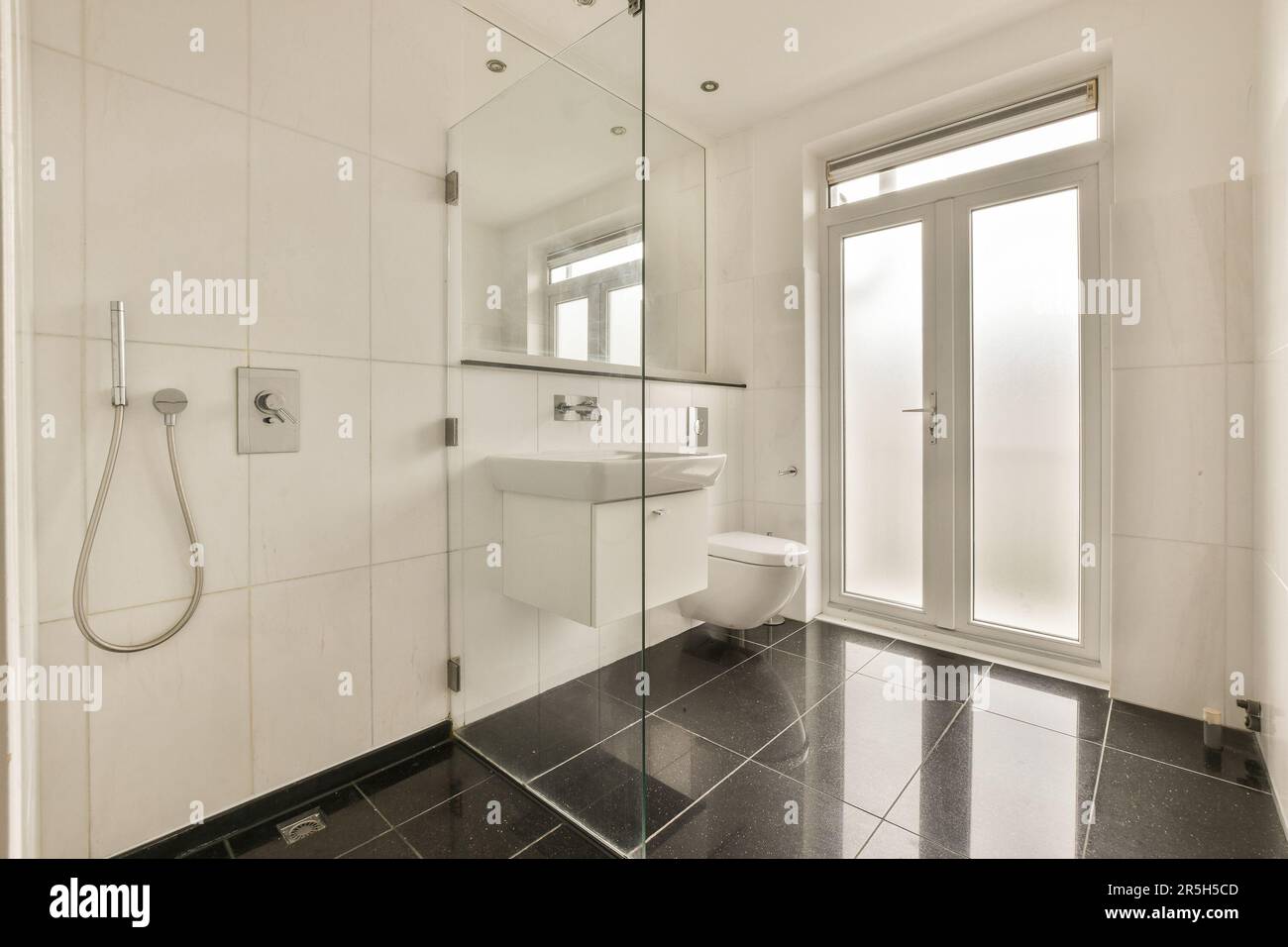 a modern bathroom with black and white tile flooring, glass shower door ...