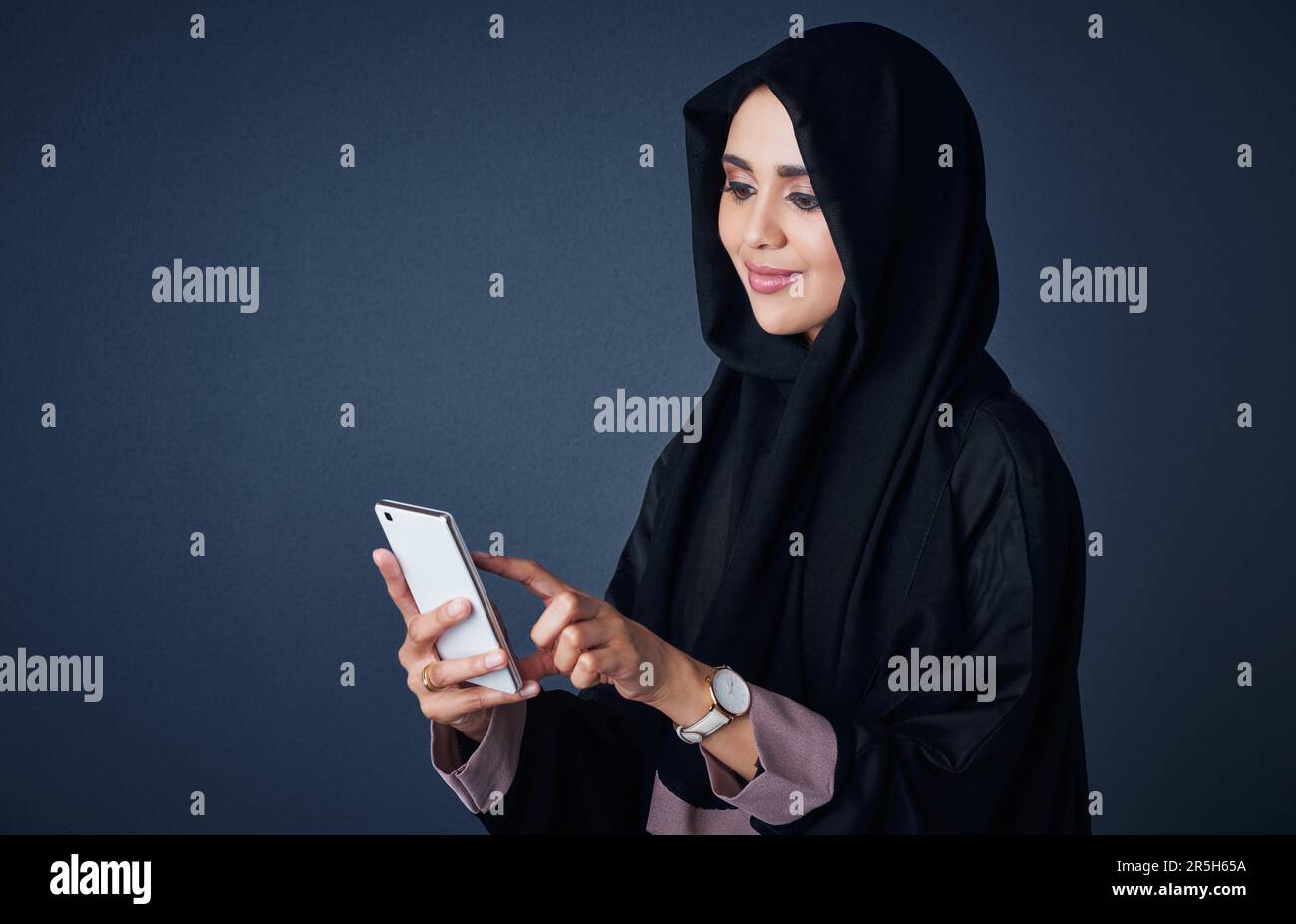 The smartest way of communication for her. Studio shot of a young woman wearing a burqa and using a mobile phone against a gray background. Stock Photo
