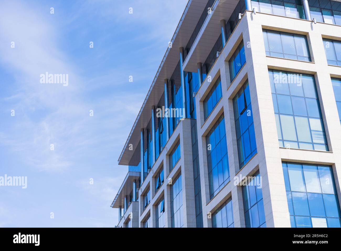 Stylish Glass Facade of blue Tinted Semi-Transparent Glass Building Against Blue Sky with Sunbeams. Modern Architecture Concept Stock Photo