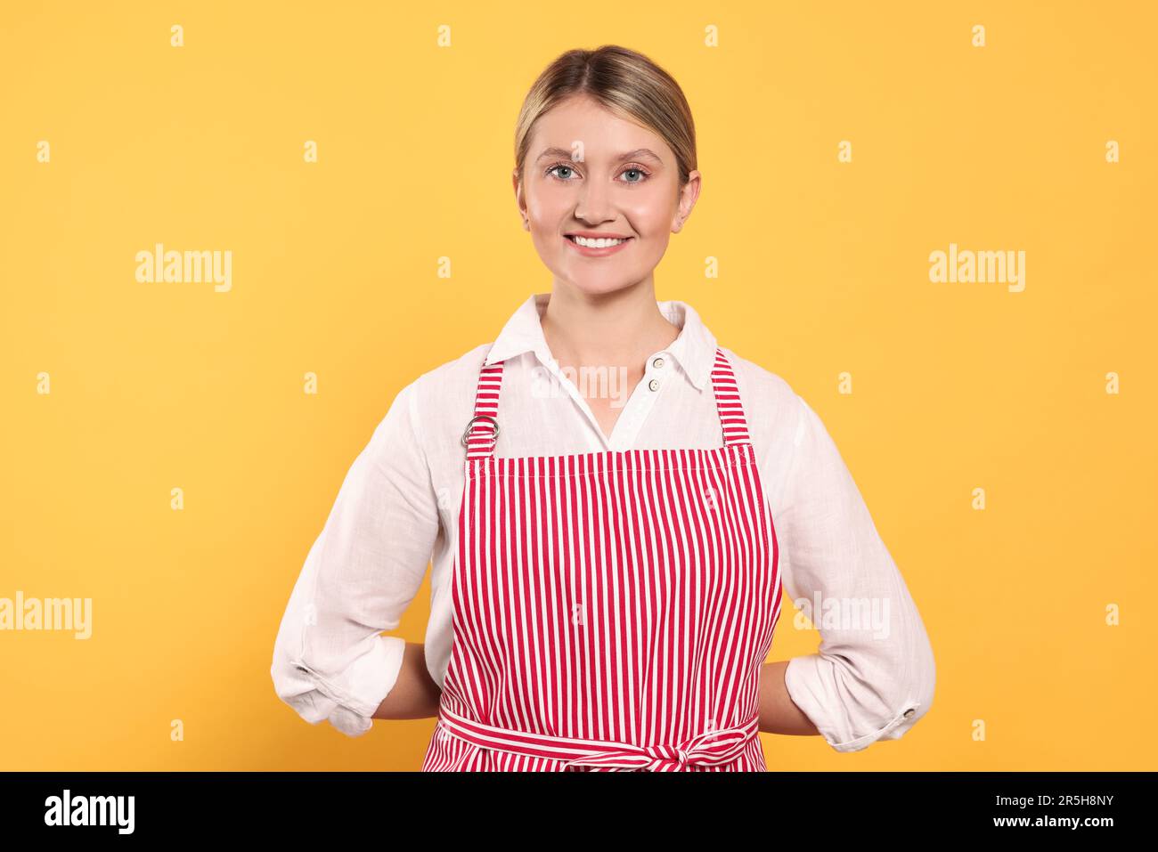 Beautiful young woman in clean striped apron on orange background Stock ...