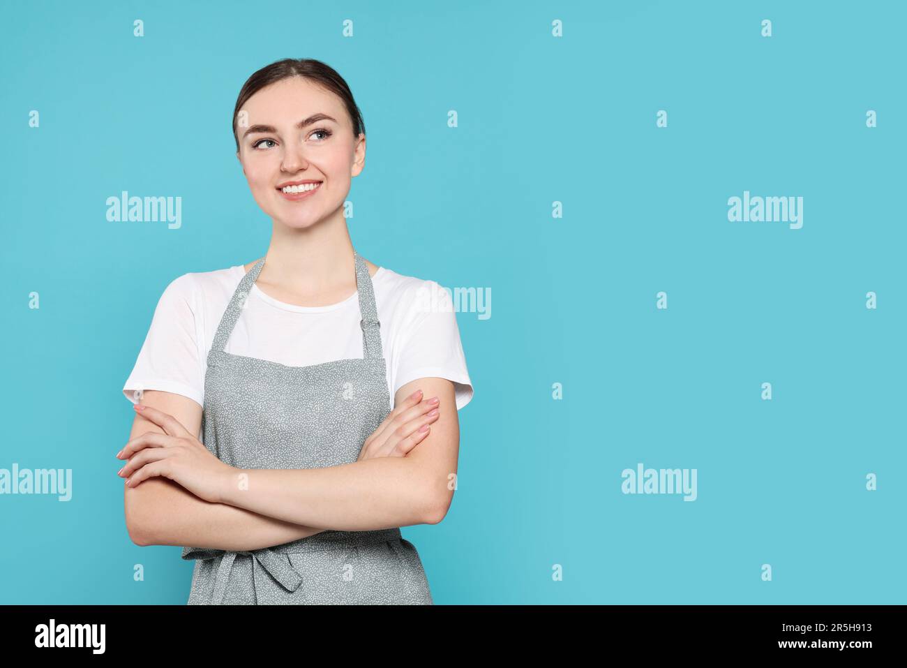 Beautiful young woman in clean apron with pattern on light blue ...
