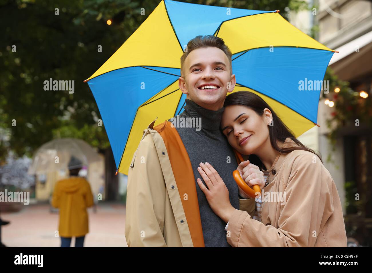 Lovely young couple with umbrella walking under rain on city street ...